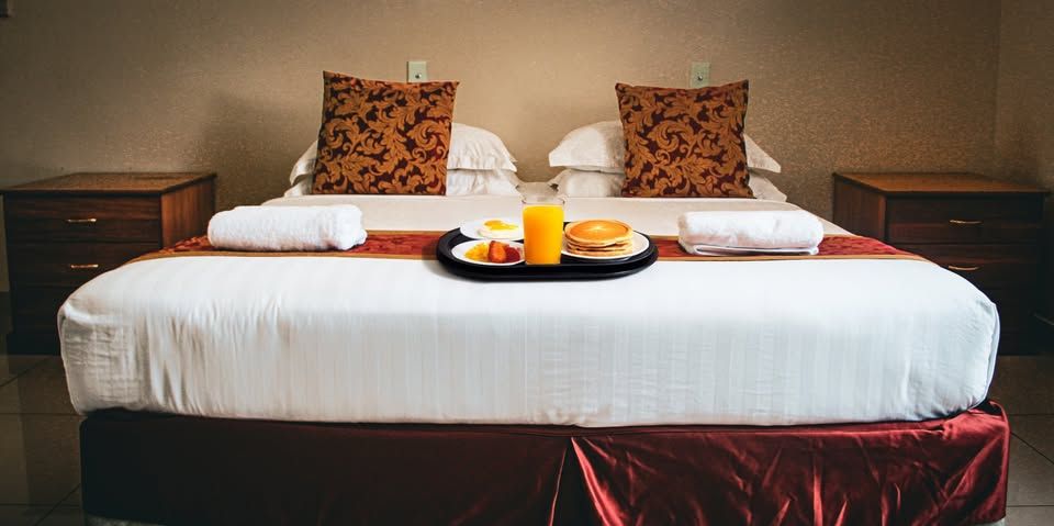 A neatly made bed with a breakfast tray featuring pancakes and juice.