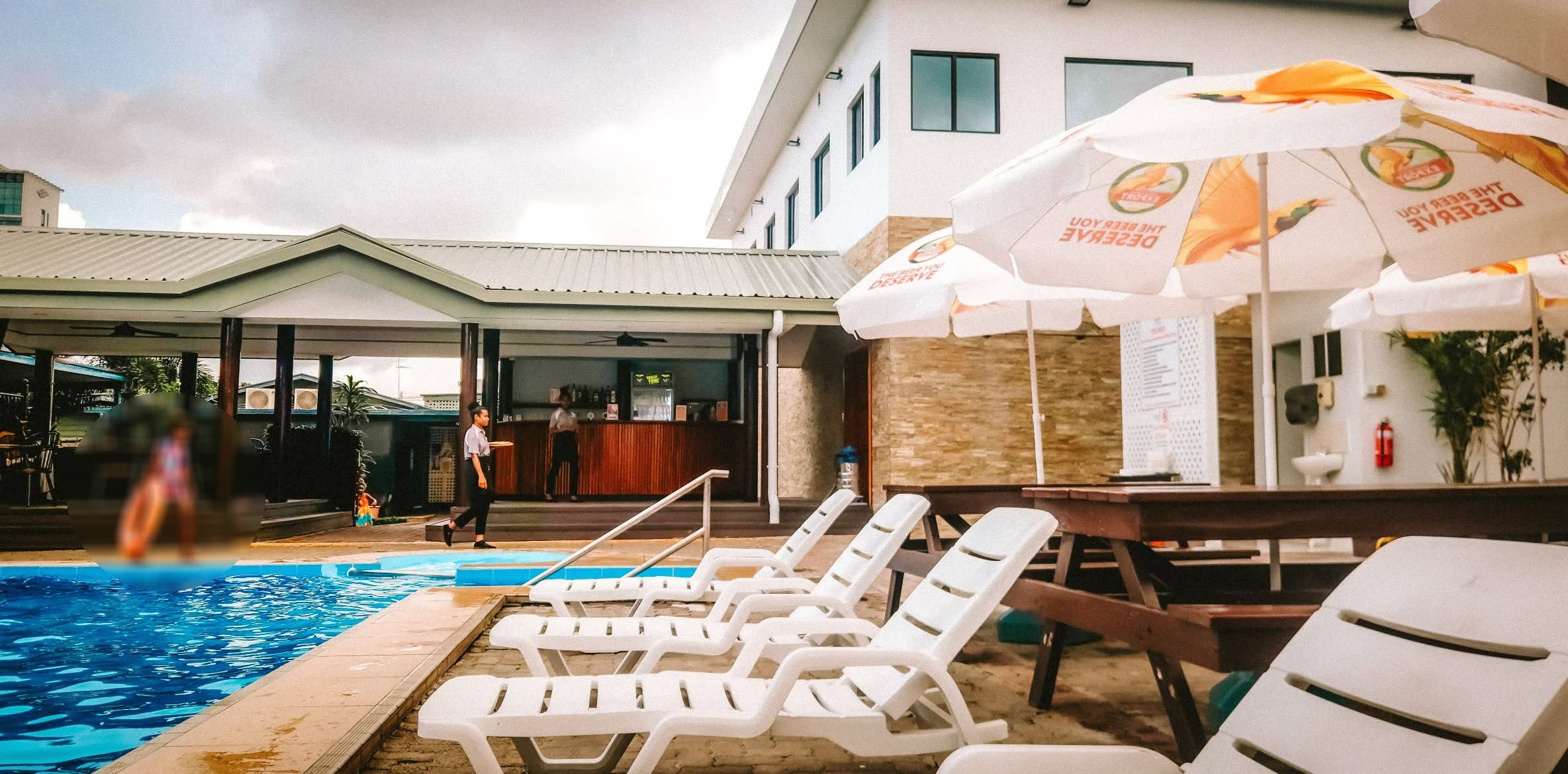 Poolside lounge area with white recliners and shaded umbrellas.