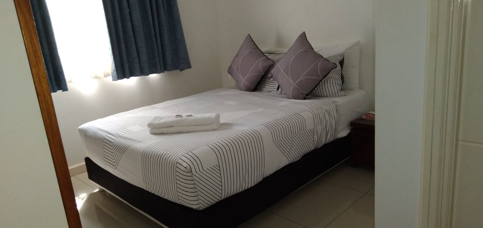 Bright guest room with a double bed, purple pillows, and blue curtains.