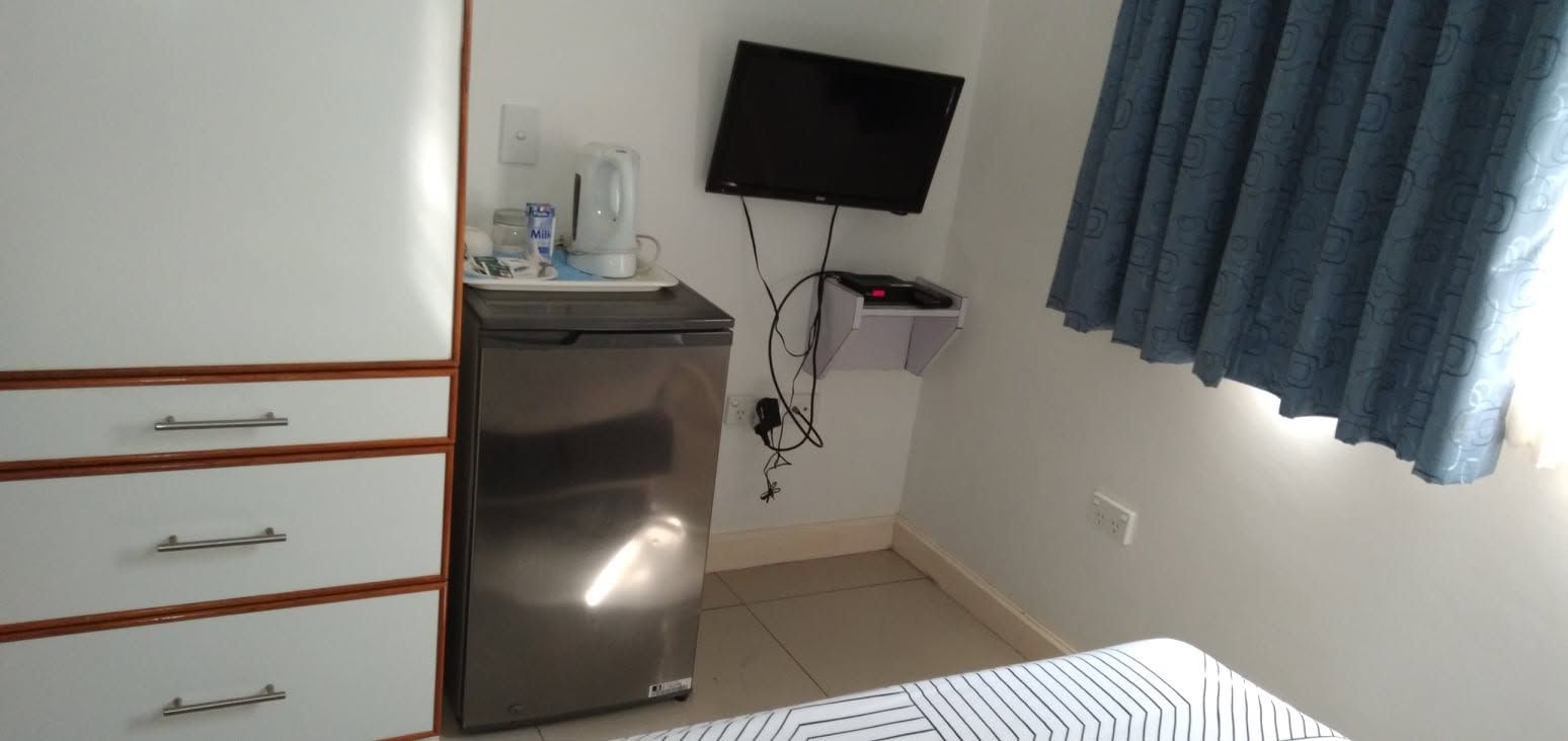Room amenities including a mini-fridge, wall-mounted TV, and white drawers.