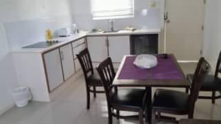 Dining area with a wooden table and dark chairs next to the kitchenette.