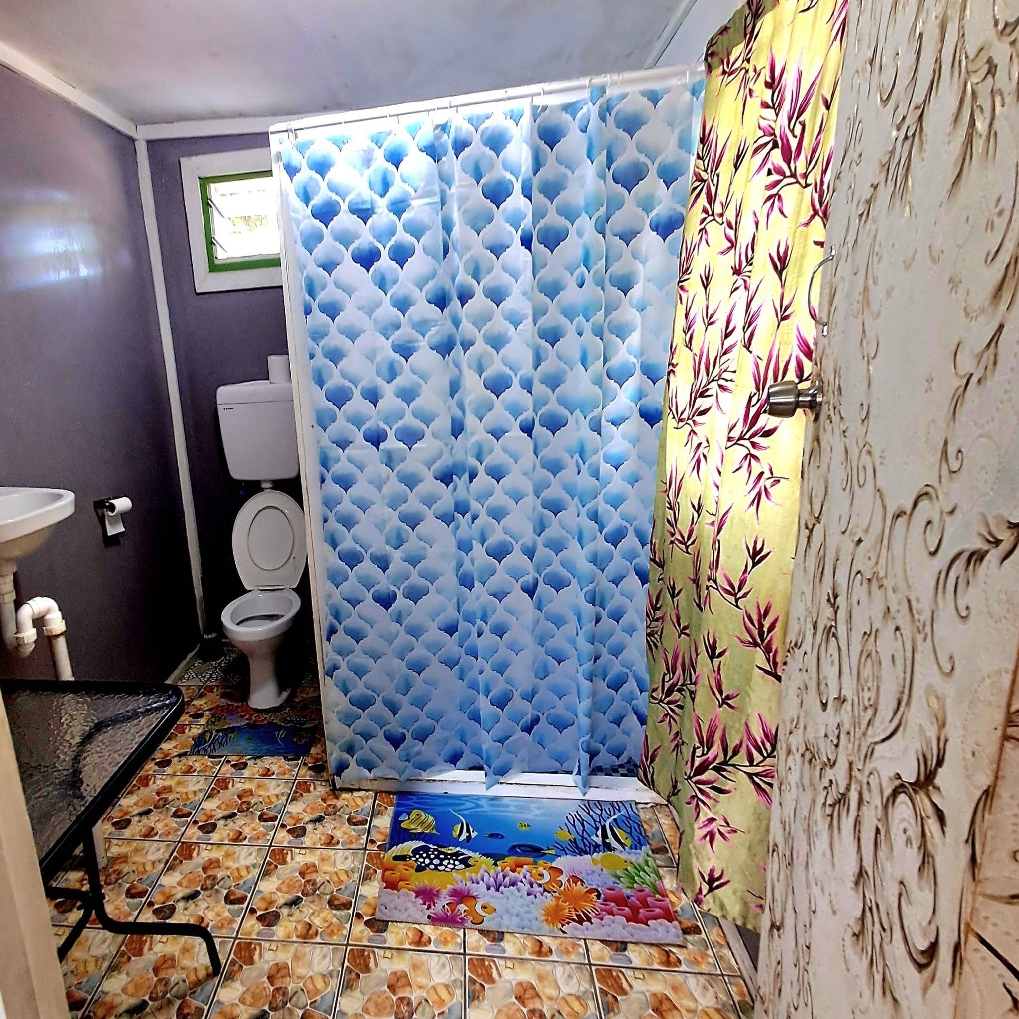 Tiled bathroom featuring a blue shower curtain and colorful mats.