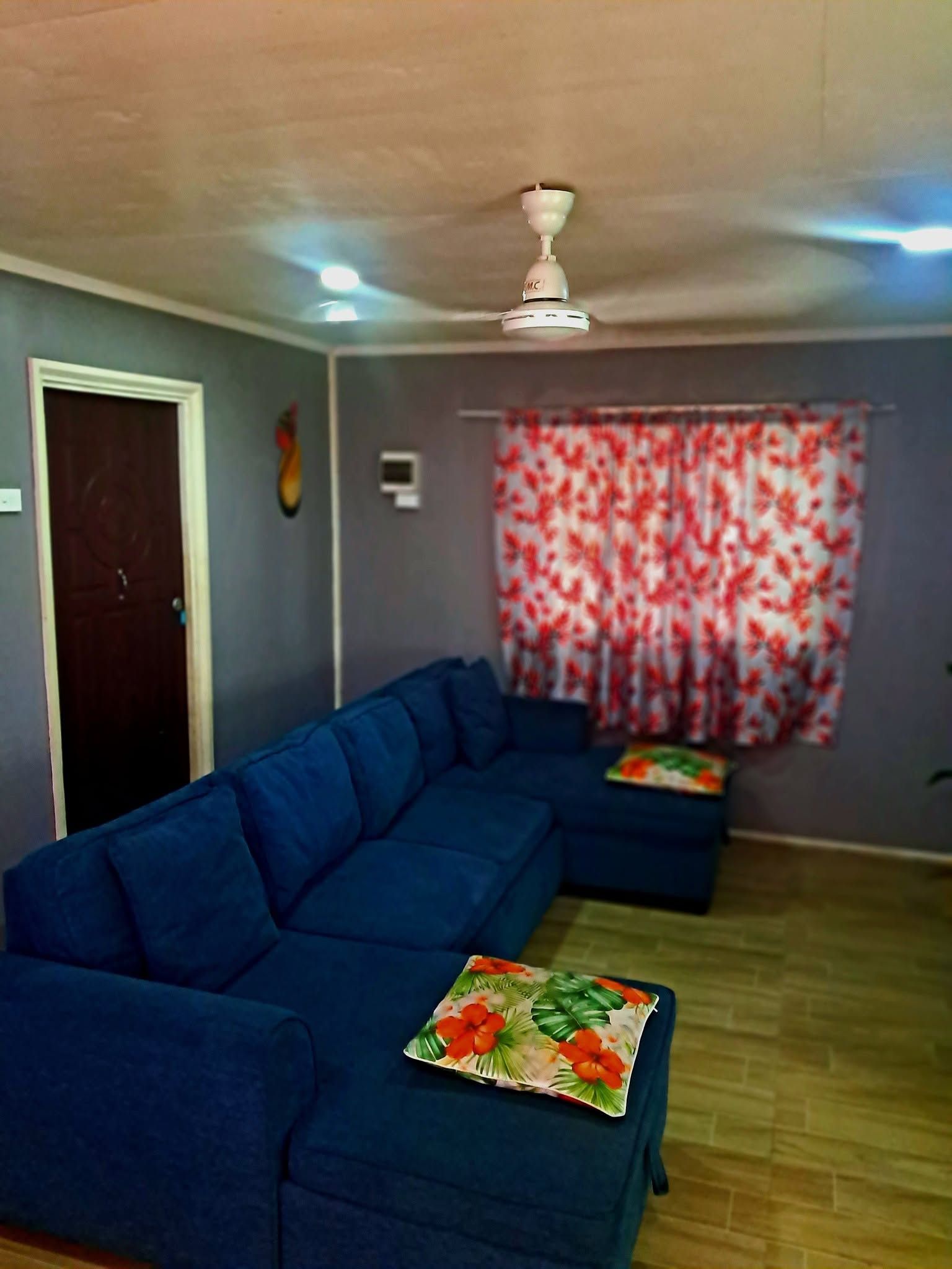 Comfortable blue corner sofa with floral cushions and ceiling fan.