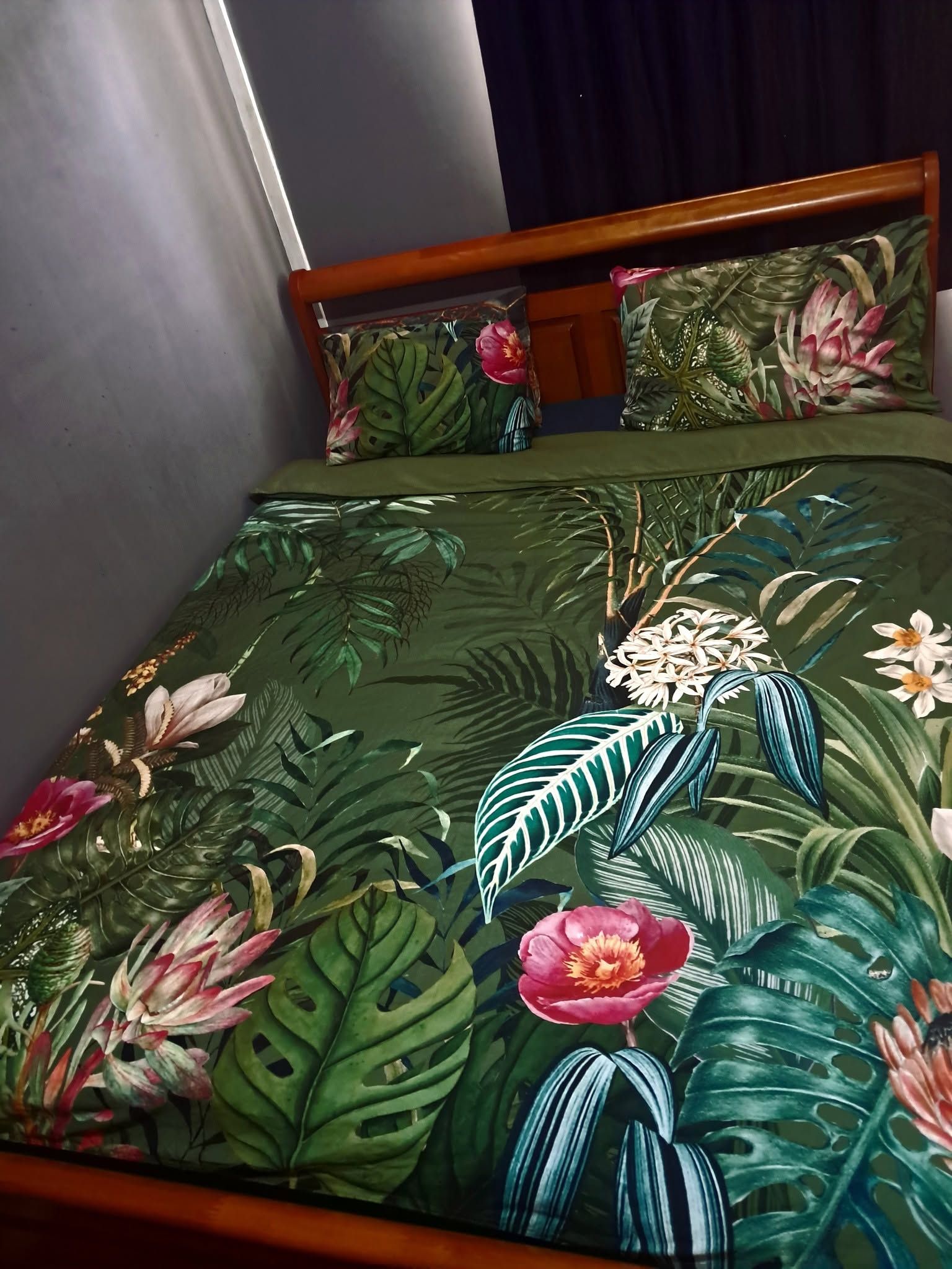 Double bed with decorative green tropical floral patterned linens.