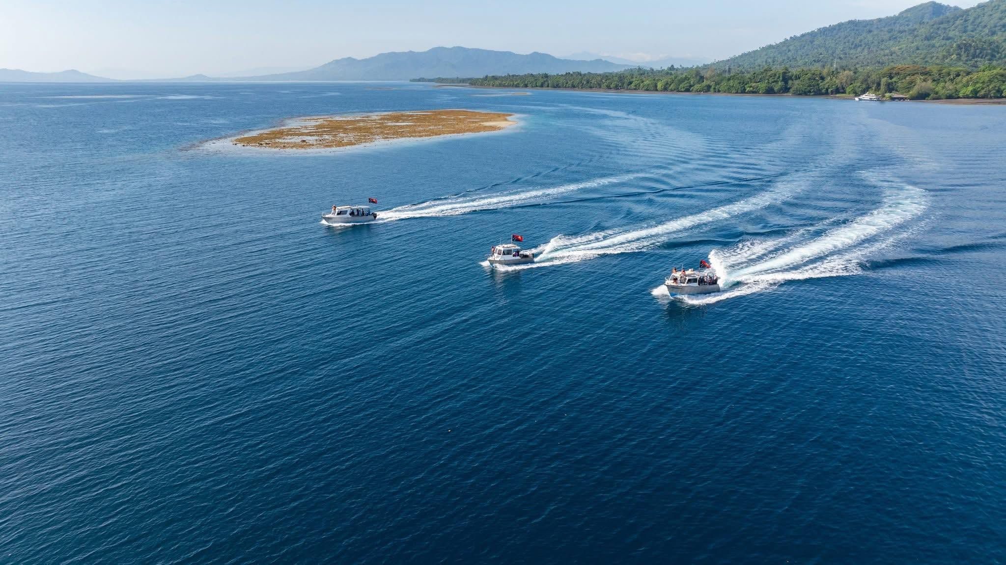 Three boats cruising across the clear blue waters of Kimbe Bay.