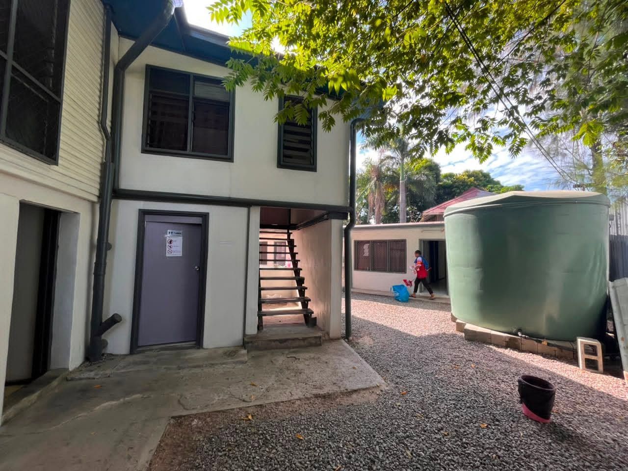 Backyard area with a large green water tank and gravel ground