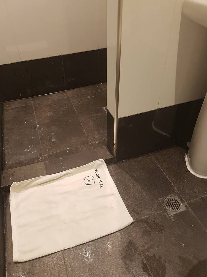 Branded floor mat on dark tiled flooring inside a guest bathroom.