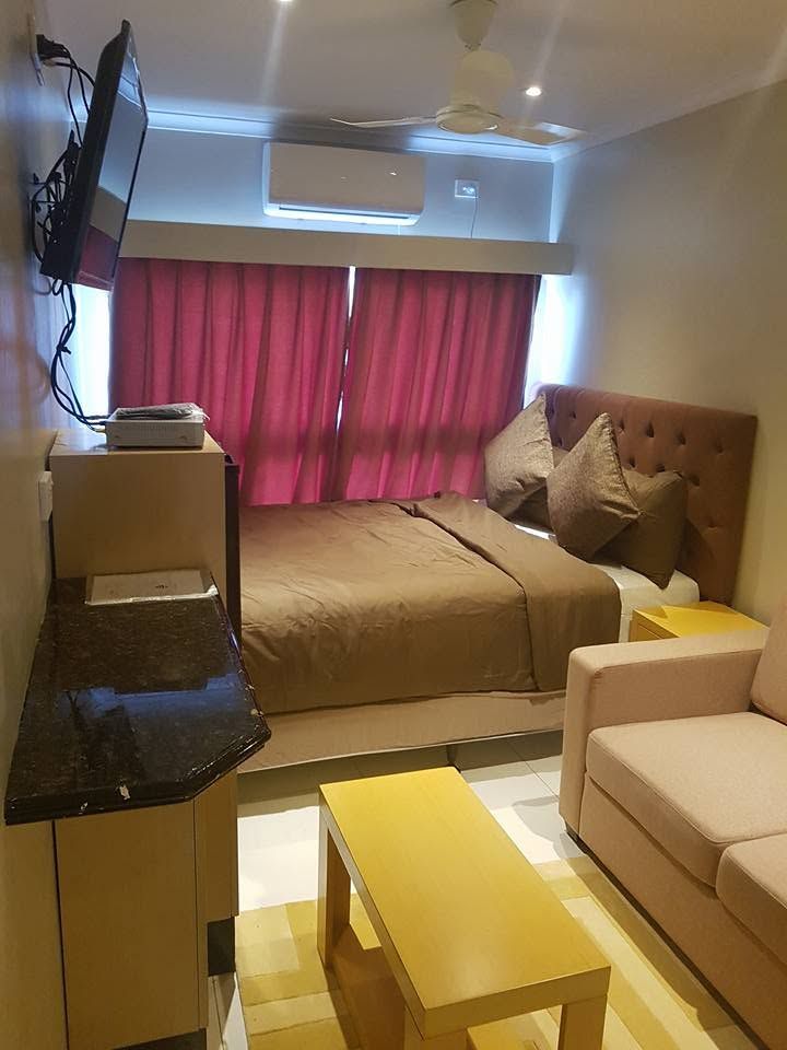 Guest room with a made bed, wall-mounted television, and a small sofa.
