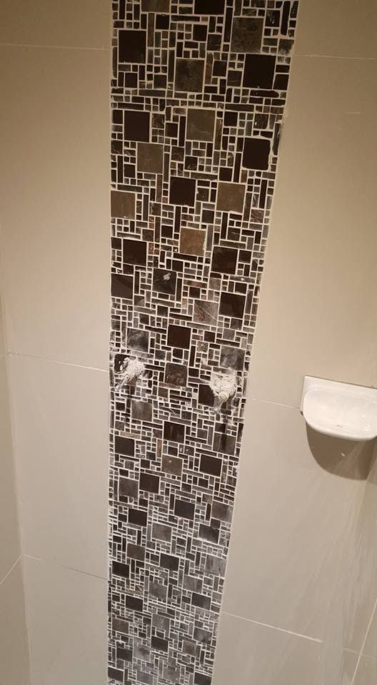 Decorative shower wall with a vertical earth-toned mosaic pattern.