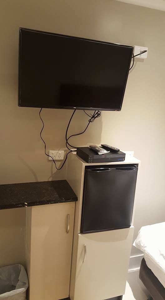 Wall-mounted flatscreen TV above a compact storage unit and mini-fridge.