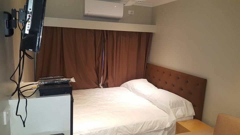 Double bed with white linens and a tufted brown headboard next to a window.