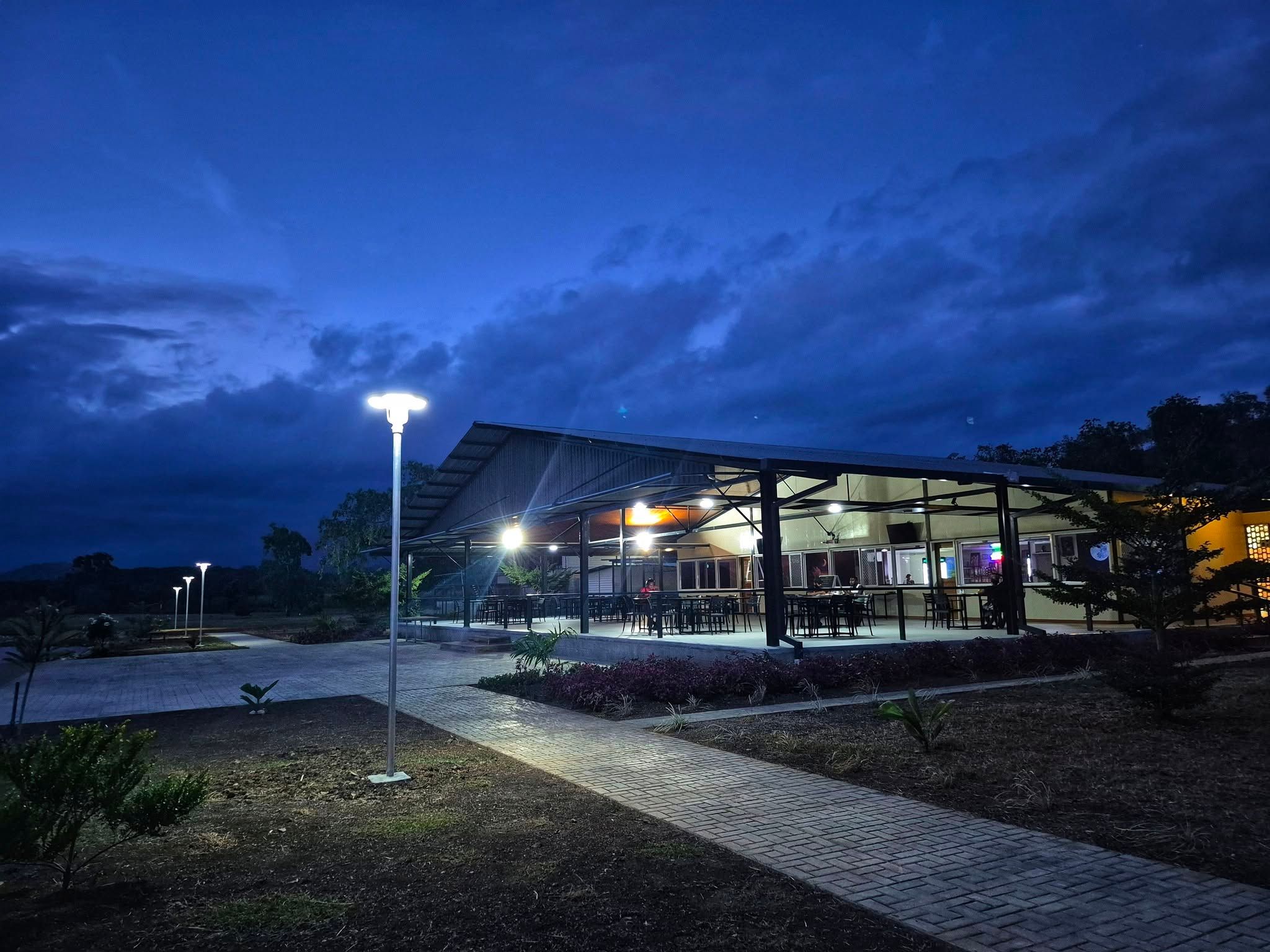 Illuminated outdoor dining area with tables and chairs under a dark evening sky.