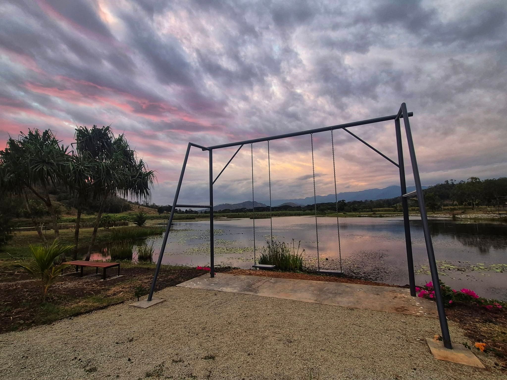 Large outdoor swing frame overlooking a serene lake during a vibrant sunset.