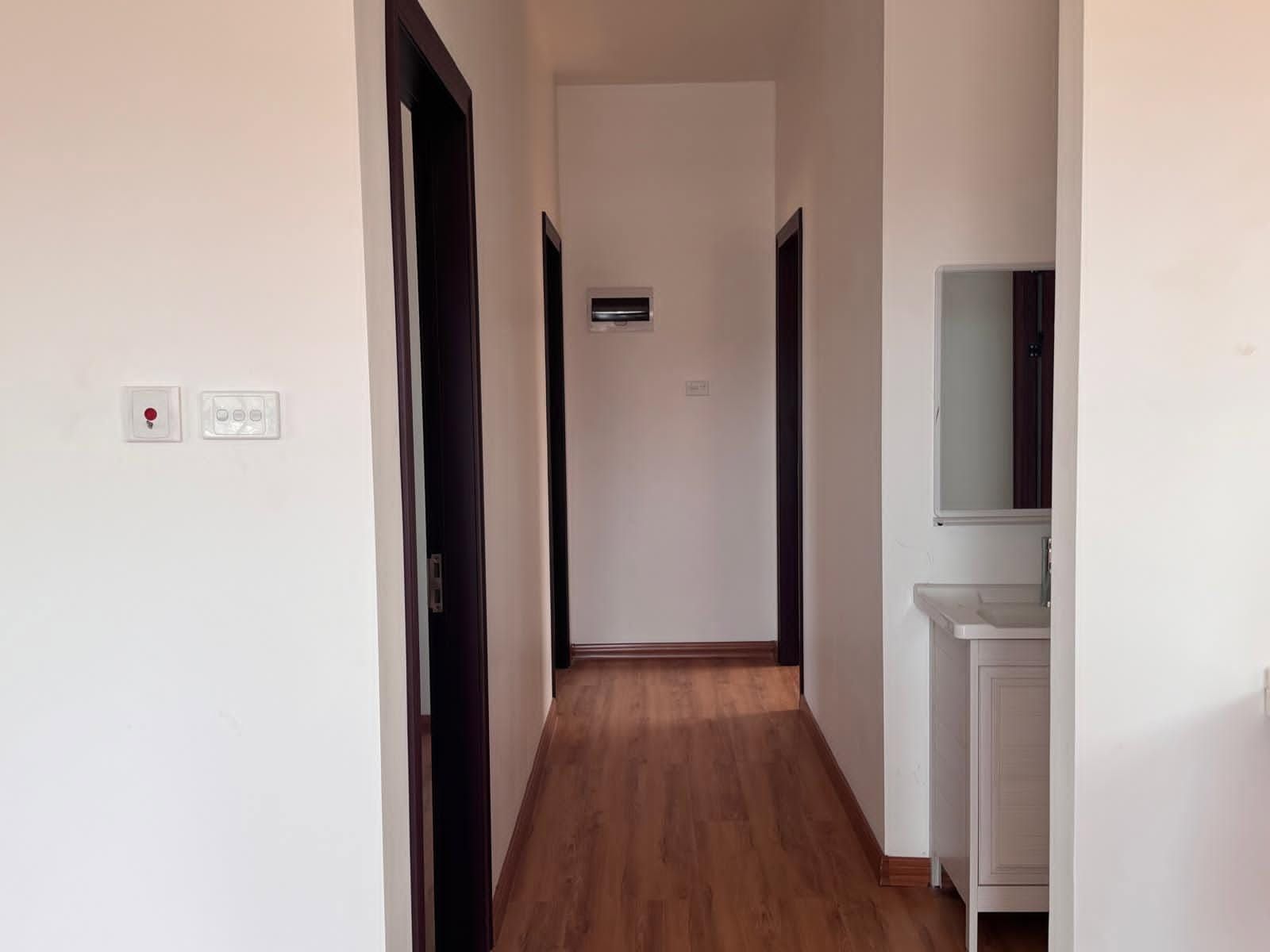 Internal hallway with wooden flooring leading to several dark-framed doorways.