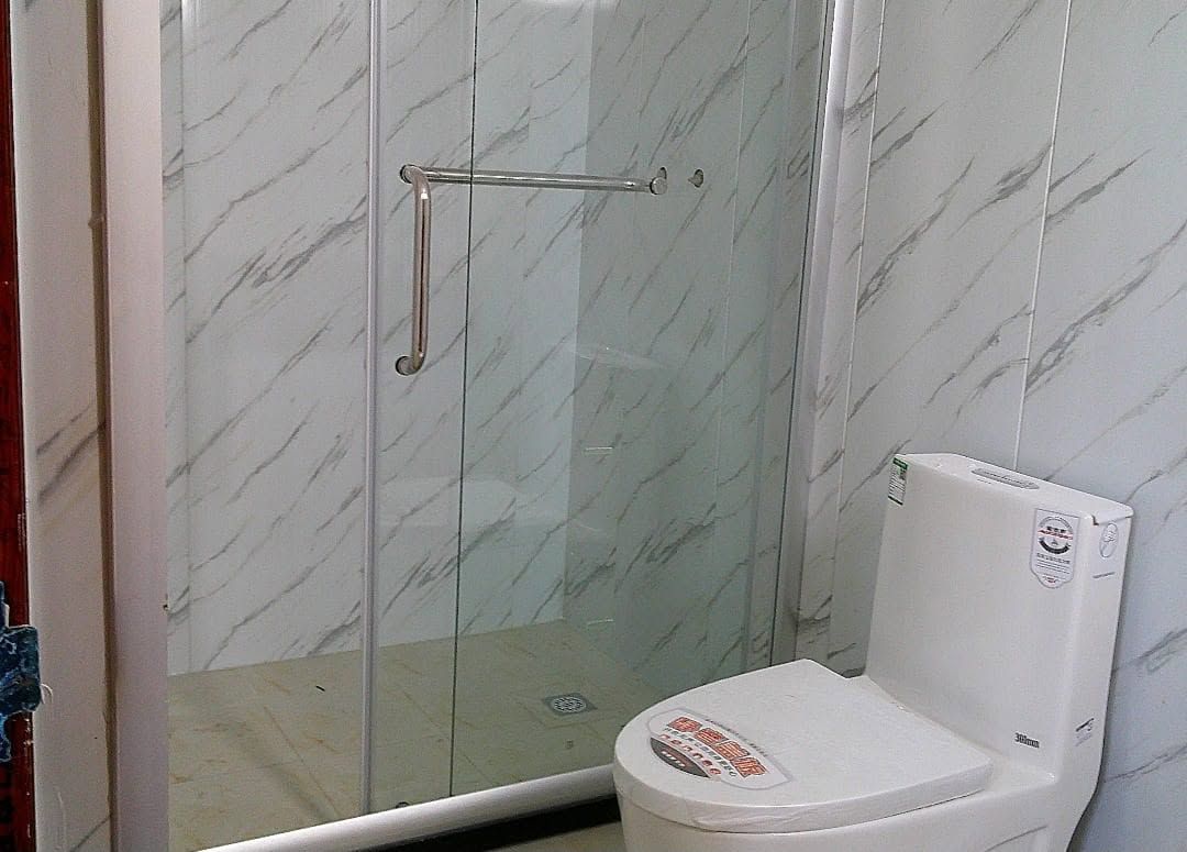 Modern bathroom featuring marble-patterned tiles, a glass shower stall, and a white toilet.