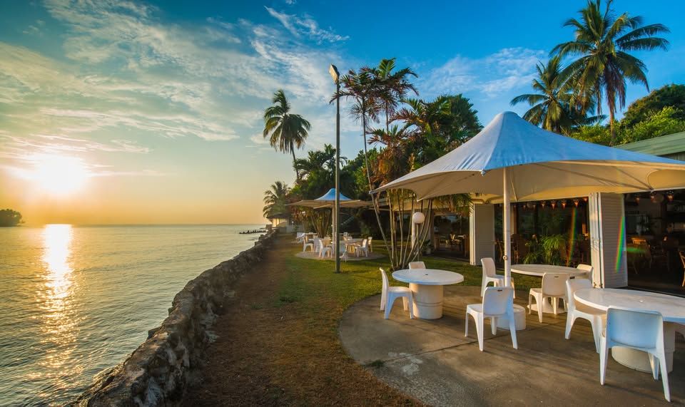 Waterfront dining area with outdoor seating under white canopies at sunset