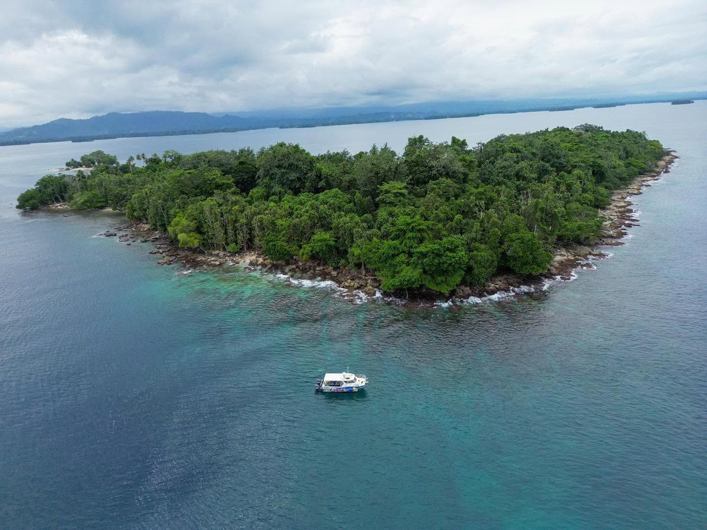 Aerial wide shot of a small island with a boat anchored nearby