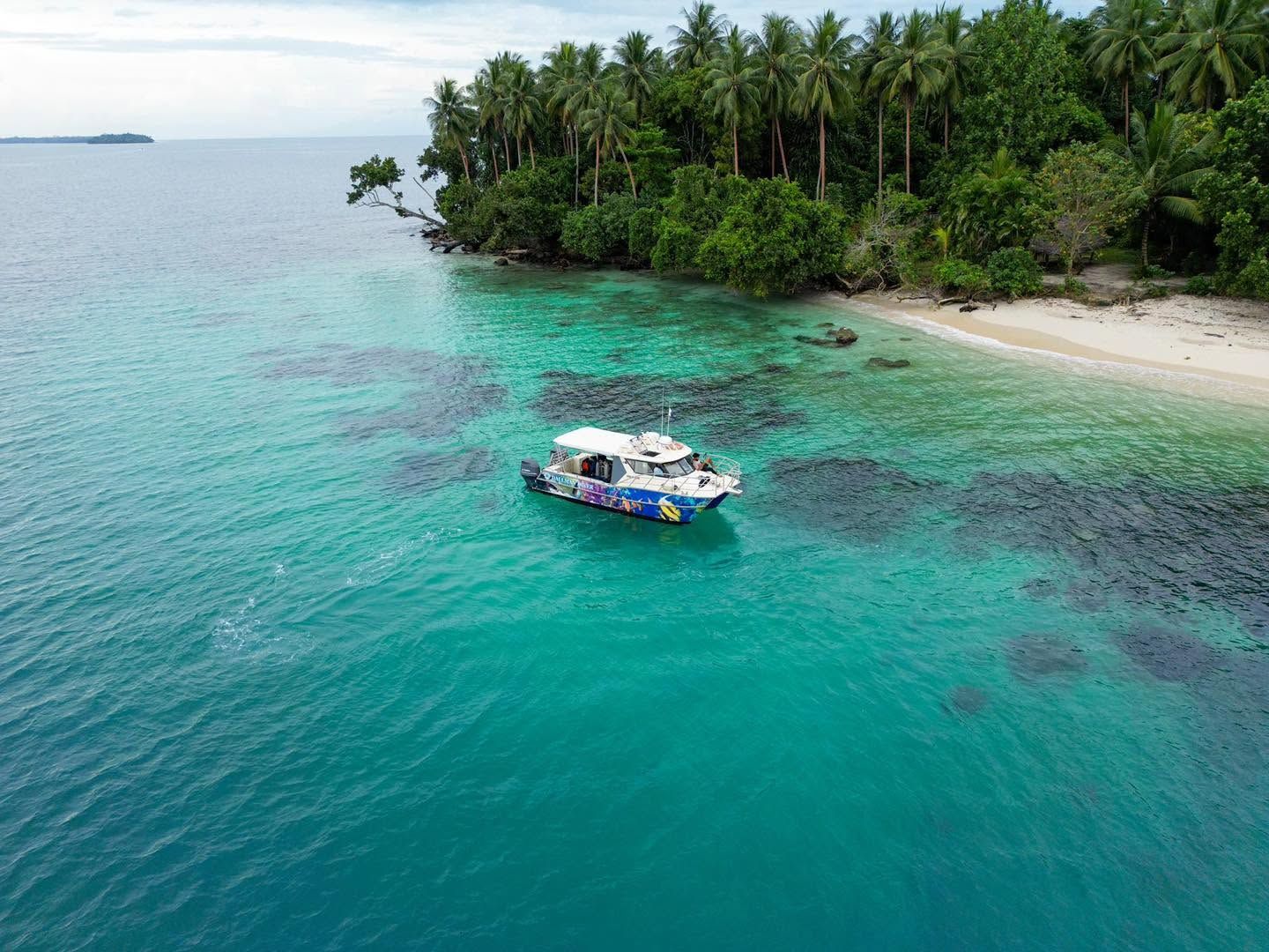 Dive boat anchored in turquoise waters near a tropical beach