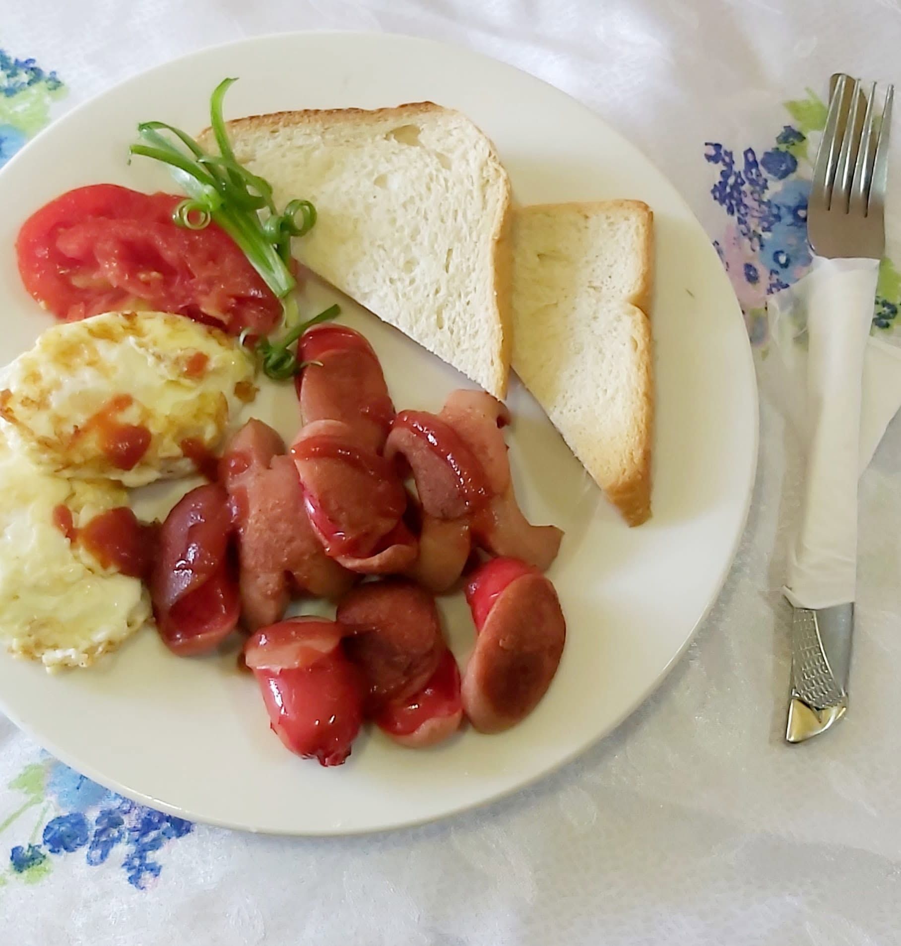 Breakfast plate with eggs, sausage, toast, and tomato.