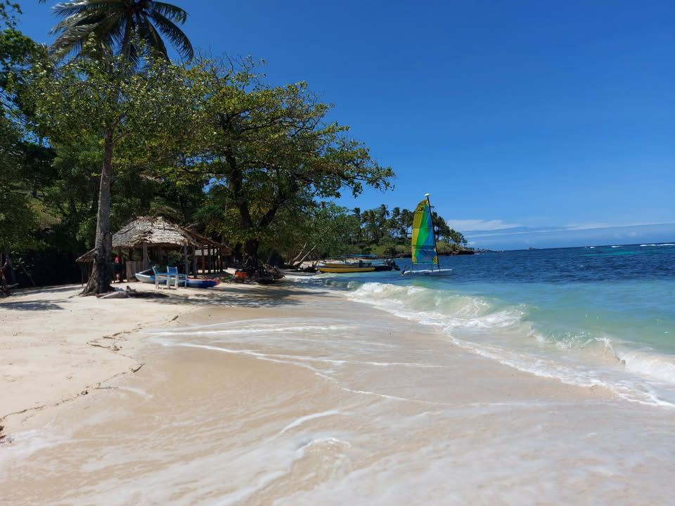 Pristine sandy beach at Tufi Resort with a sailboat on the water.